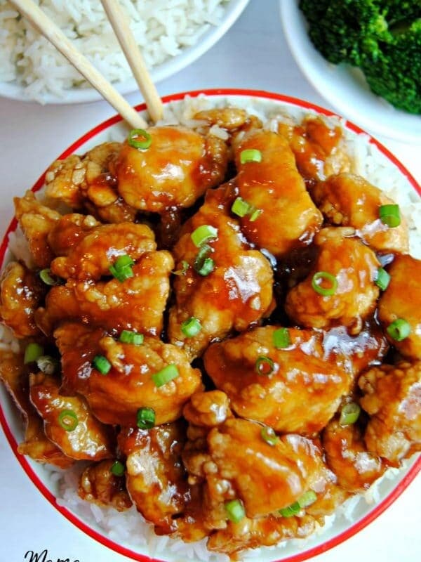 a bowl of gluten-free apricot chicken with chopsticks, broccoli and rice in the background