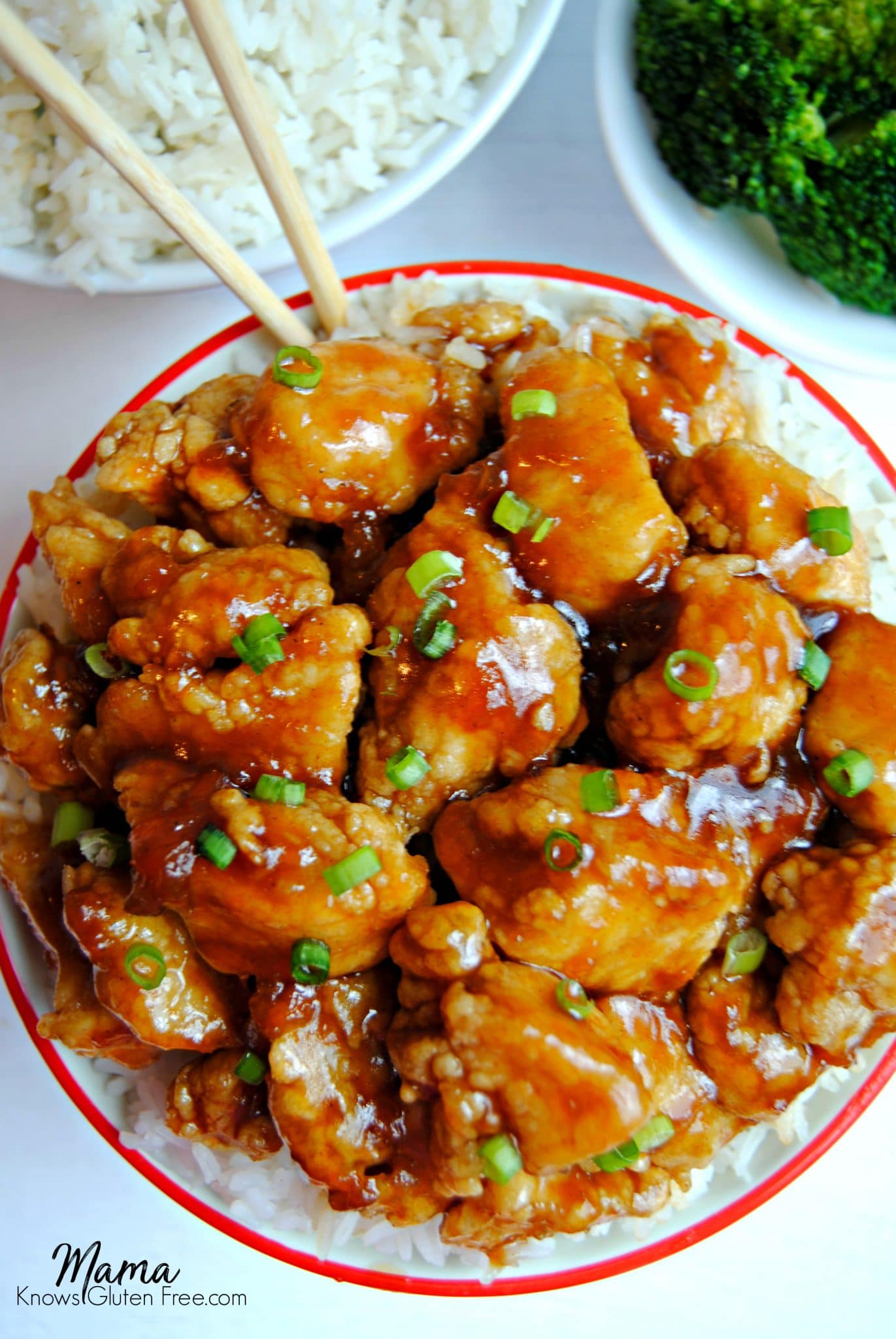 a bowl of gluten-free apricot chicken with chopsticks, rice and broccoli in the background
