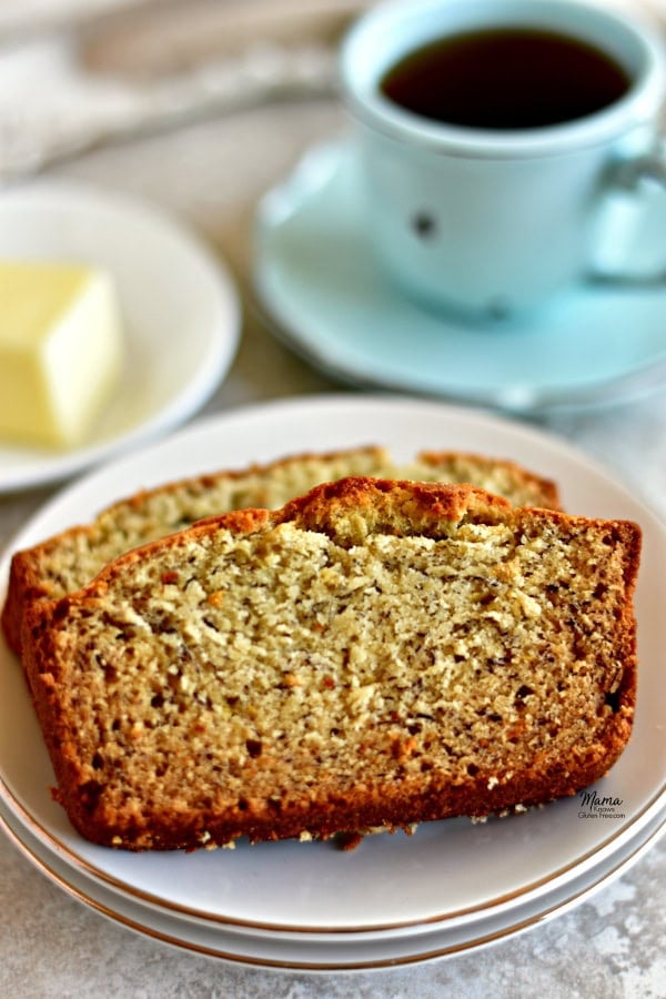 2 slices of gluten-free banana bread on a plate with coffee cup and butter in the background