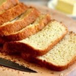 loaf of homemade gluten-free bread made in a bread machine on a cutting board with a knife and butter in the background