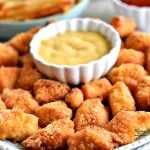 plate of gluten-free chicken nuggets and honey mustard with fries and ketchup in the background