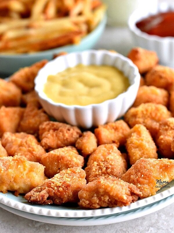 plate of gluten-free chicken nuggets and honey mustard with fries and ketchup in the background