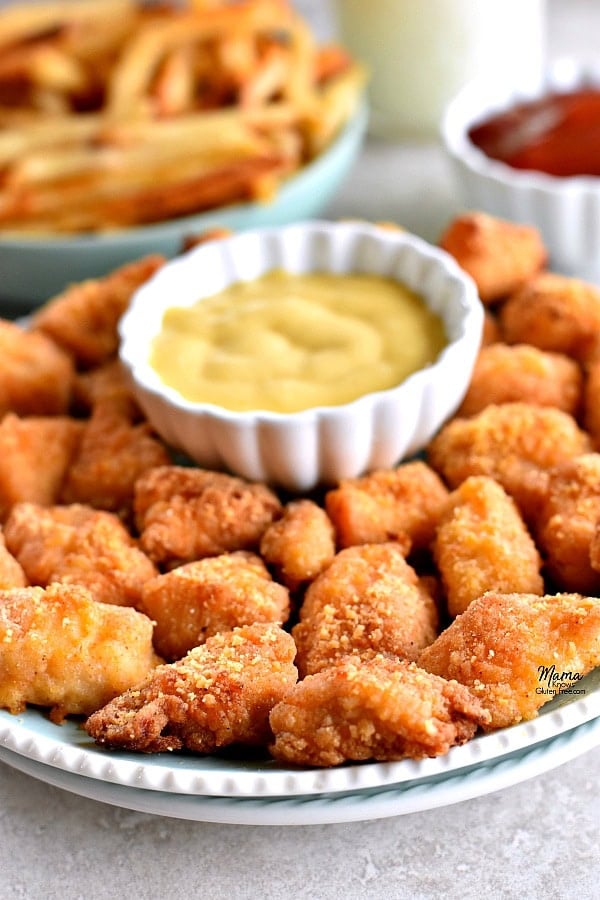 plate of gluten-free chicken nuggets and honey mustard with fries and ketchup in the background