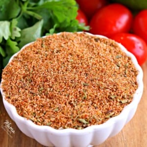 a bowl of gluten-free homemade taco seasoning with tomatoes, cilantro and avocado in the background