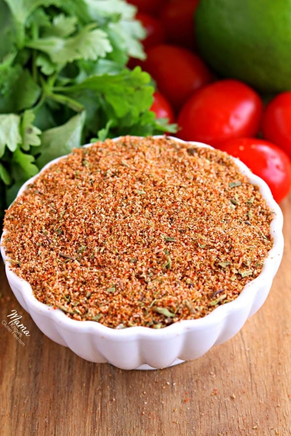 bowl of homemade gluten-free taco seasoning with cilantro, tomatoes and an avocado in the background