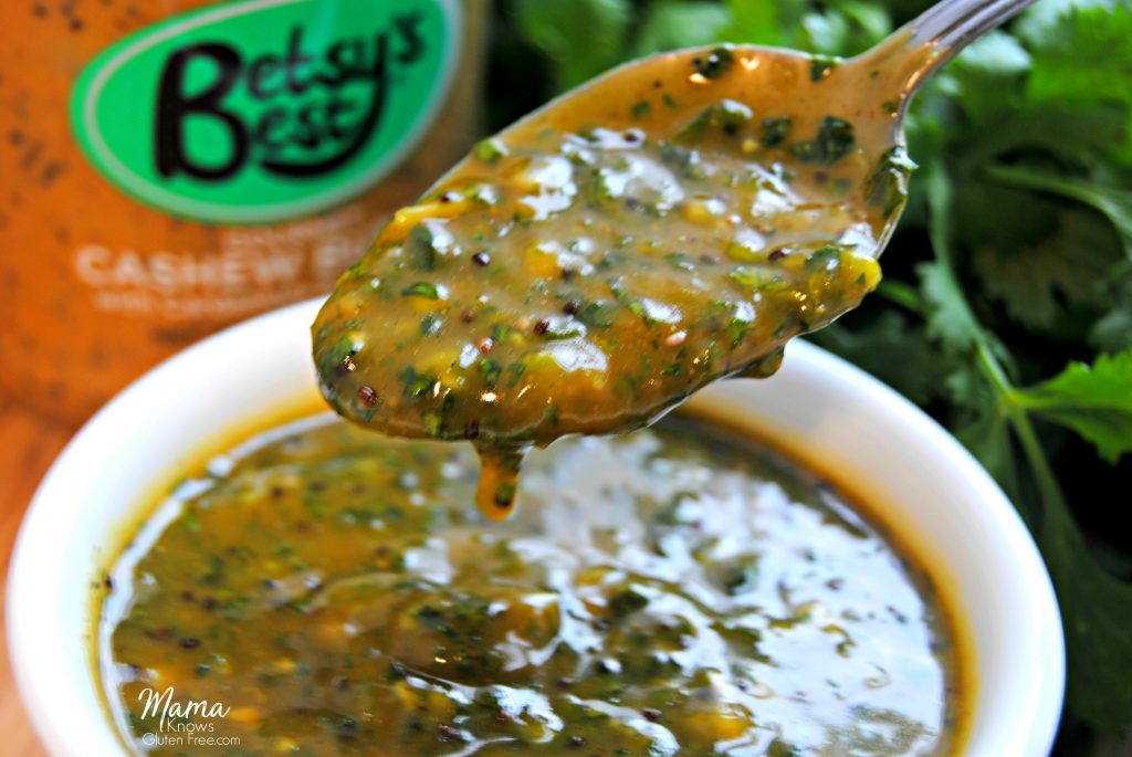 Chimichurri Sauce shown on a spoon with cashew butter and cilantro in the background