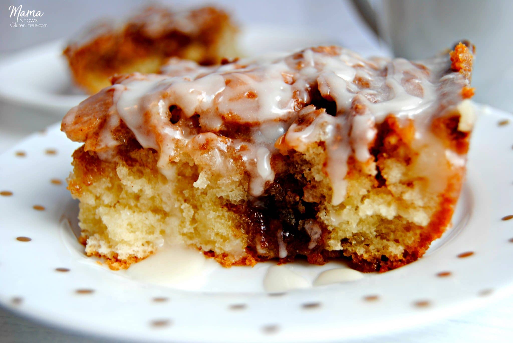 two slices of gluten-Free cinnamon roll cake on white plates with a white coffee cup. 