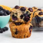 Gluten-free blueberry banana muffins stacked with one muffin sliced in half to show the soft, moist interior filled with blueberries.