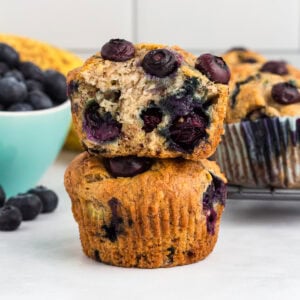 Gluten-free blueberry banana muffins stacked with one muffin sliced in half to show the soft, moist interior filled with blueberries.