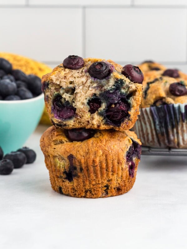 Gluten-free blueberry banana muffins stacked with one muffin sliced in half to show the soft, moist interior filled with blueberries.
