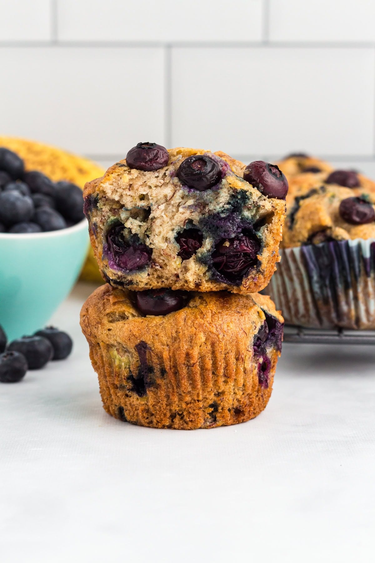Gluten-free blueberry banana muffins stacked with one muffin sliced in half to show the soft, moist interior filled with blueberries.