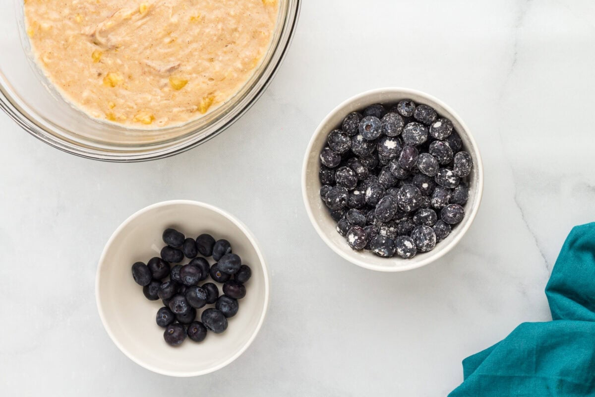 Blueberries coated in gluten-free flour beside banana muffin batter before folding into the mixture.