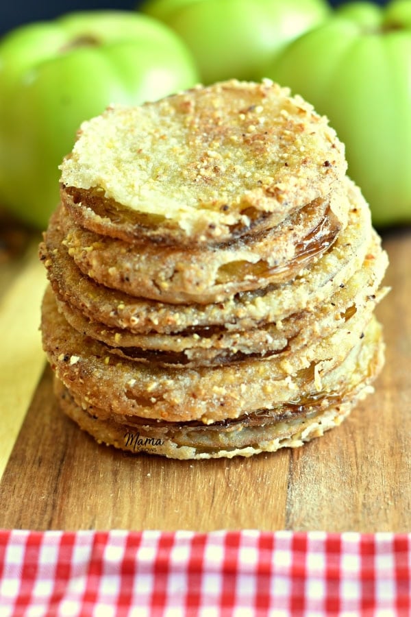 4 gluten-free fried green tomatoes stacked on top of each other with green tomatoes in the background