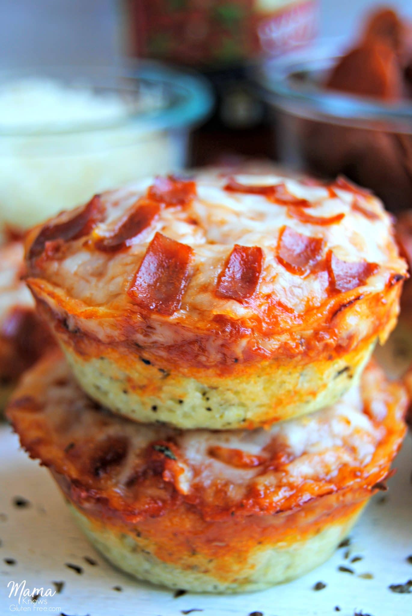2 gluten-free pizza bites stacked on top of each other with toppings in the background