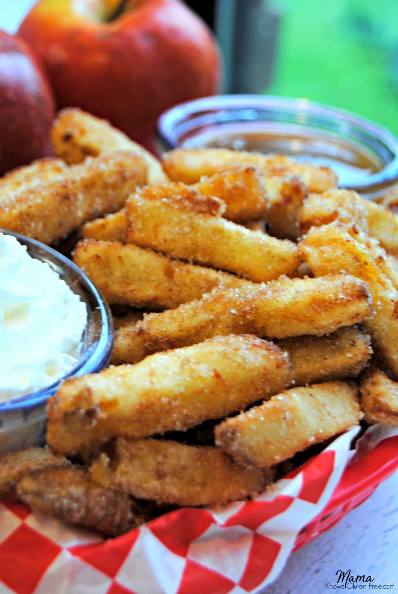  cinnamon apple fries in a basket with whipped cream and caramel dipping sauce with red apples in the background 