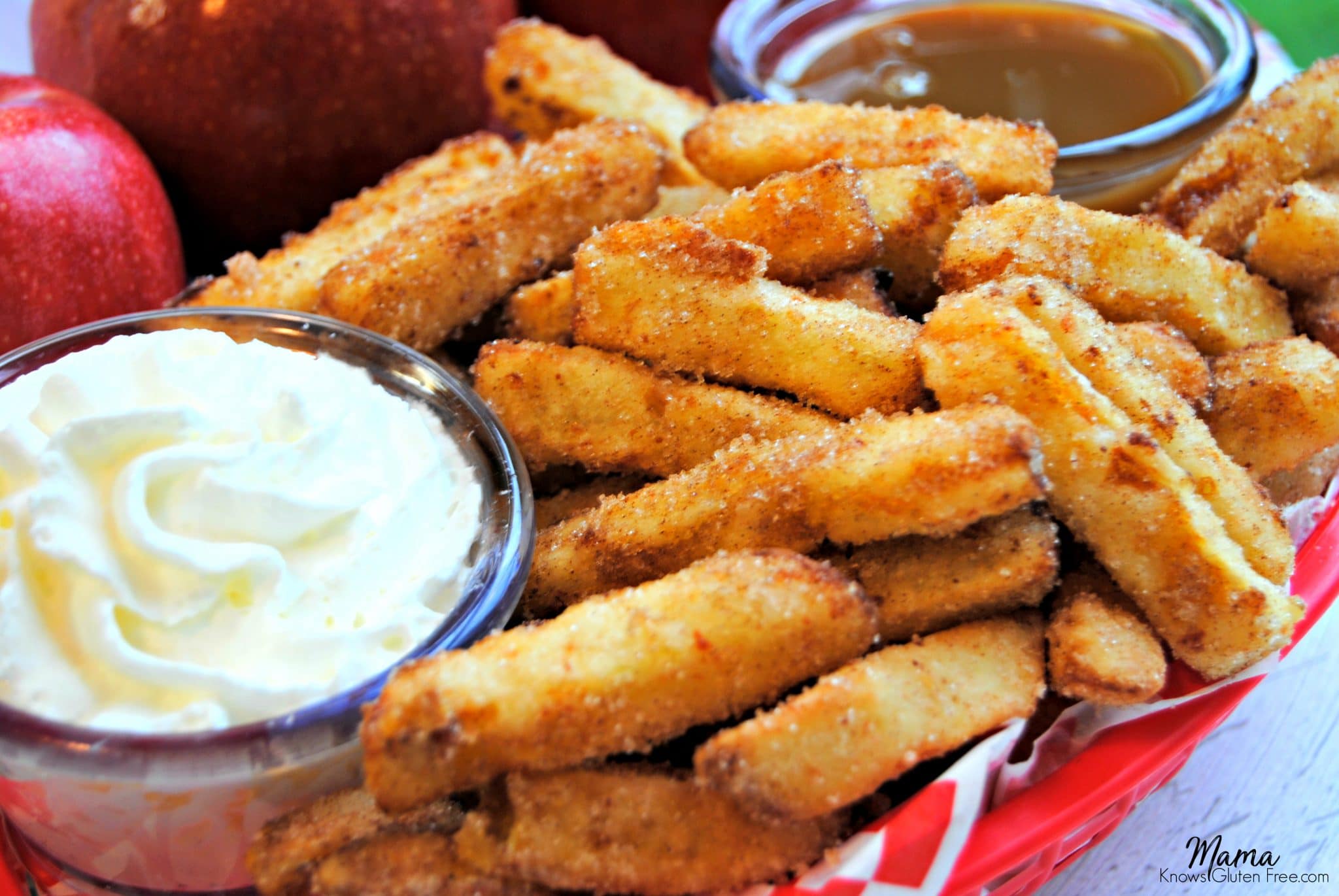  cinnamon apple fries in a basket with whipped cream and caramel dipping sauce with red apples in the background 