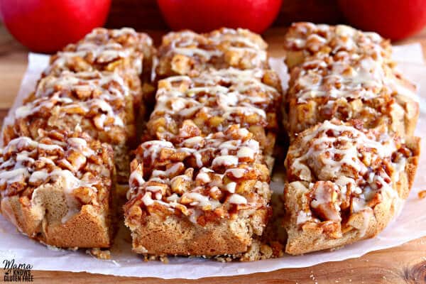 Nine gluten-free apple pie blondies on white parchment paper and a cutting board with three red apples in the background.