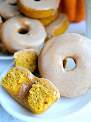 Gluten-Free Baked Pumpkin Donuts on a white plate with pumpkin is the background