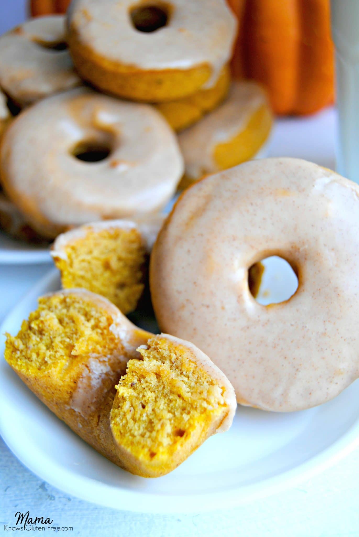 Gluten-Free Baked Pumpkin Donuts on a white plate with pumpkin is the background