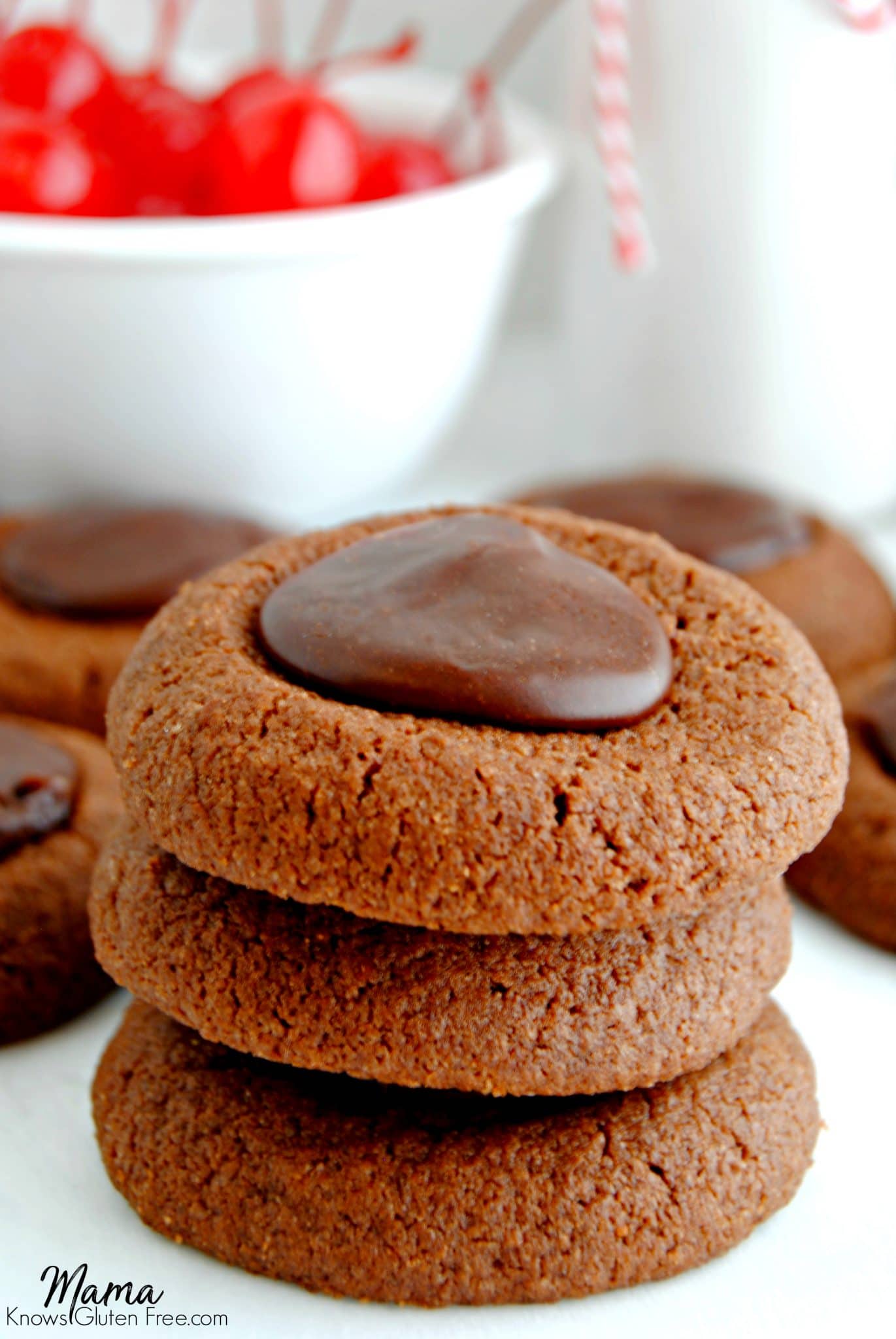 Gluten-Free Chocolate Cherry Thumbprint Cookies stacked on top of each other with cherries in the background