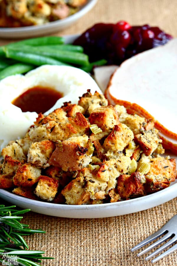 gluten-free stuffing with turkey, mashed potatoes and gravy, green beans and cranberry sauce on a white plate