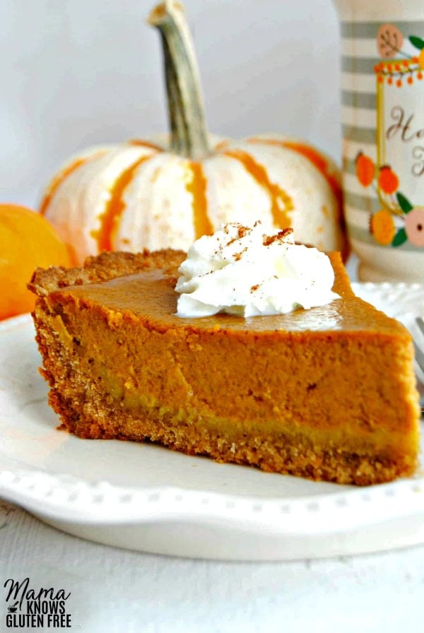 slice of gluten-free pumpkin pie topped with whipped cream with 2 pumpkins and a coffee cup in the background