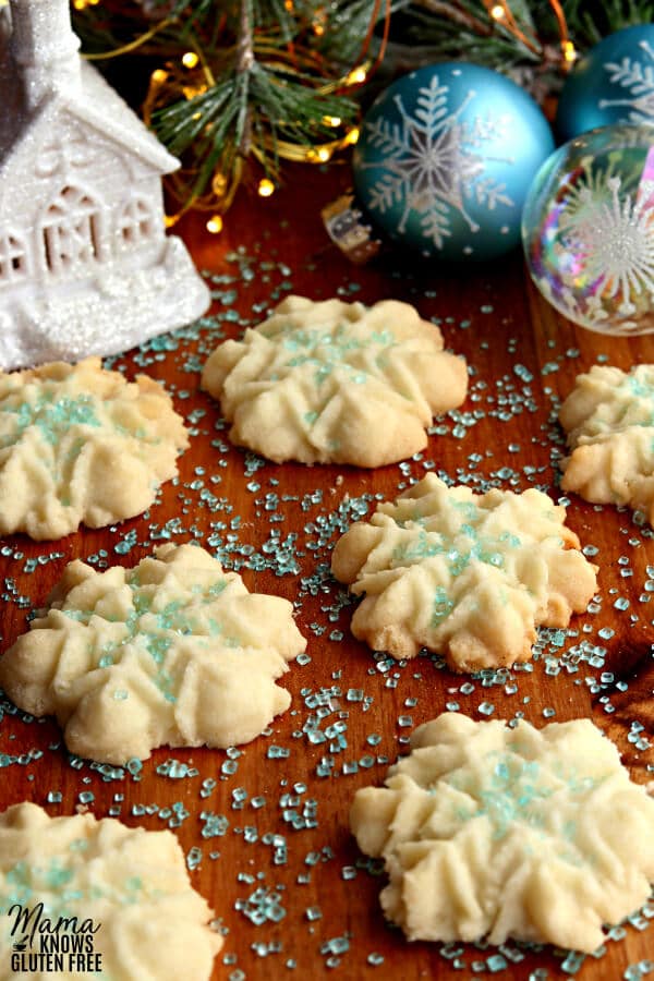 gluten-free almond spritz cookies with blue sprinkles and Christmas ornaments in the background.