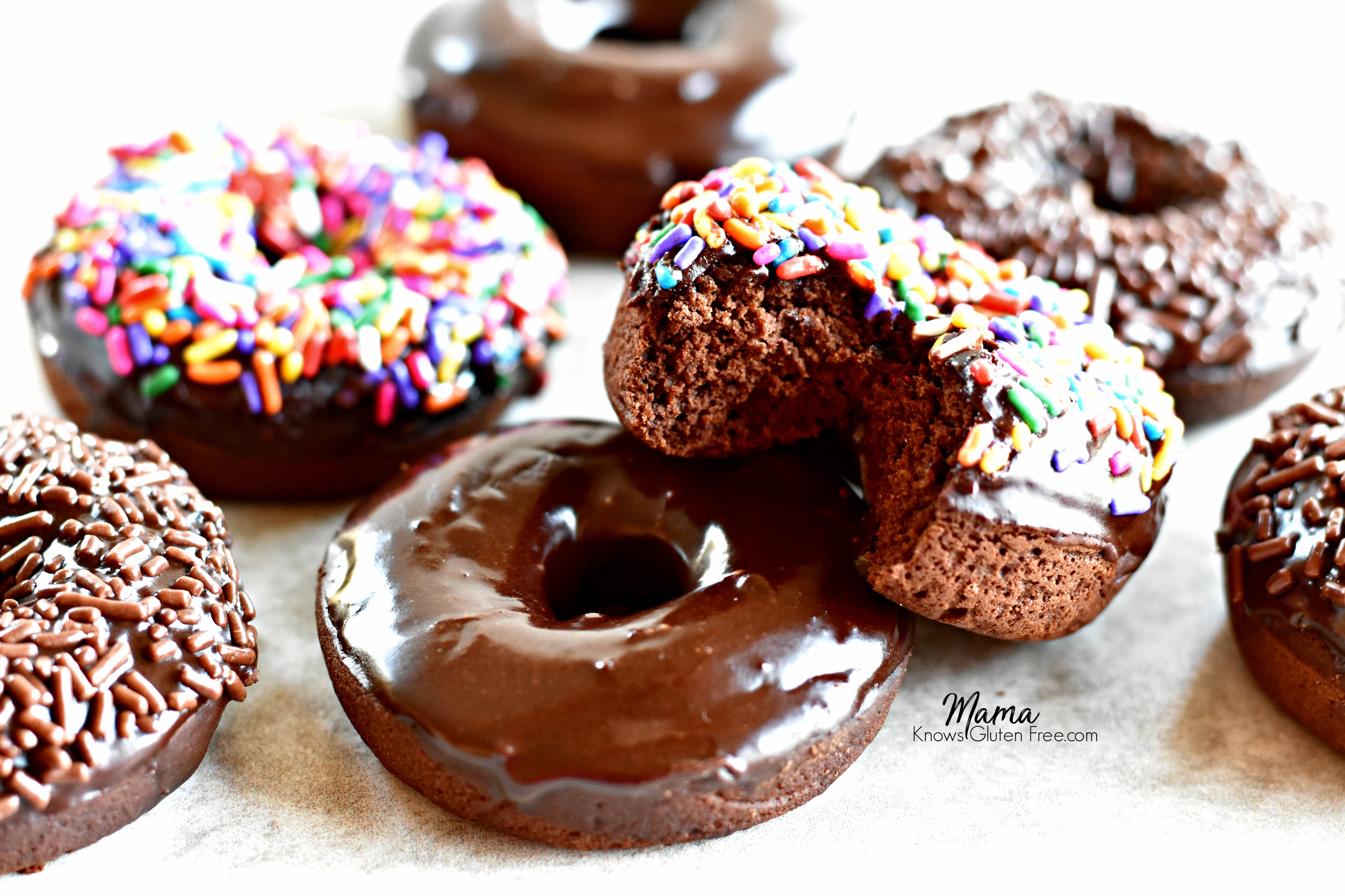 7 gluten-free baked chocolate donuts with one with a bite out of it to show the texture
