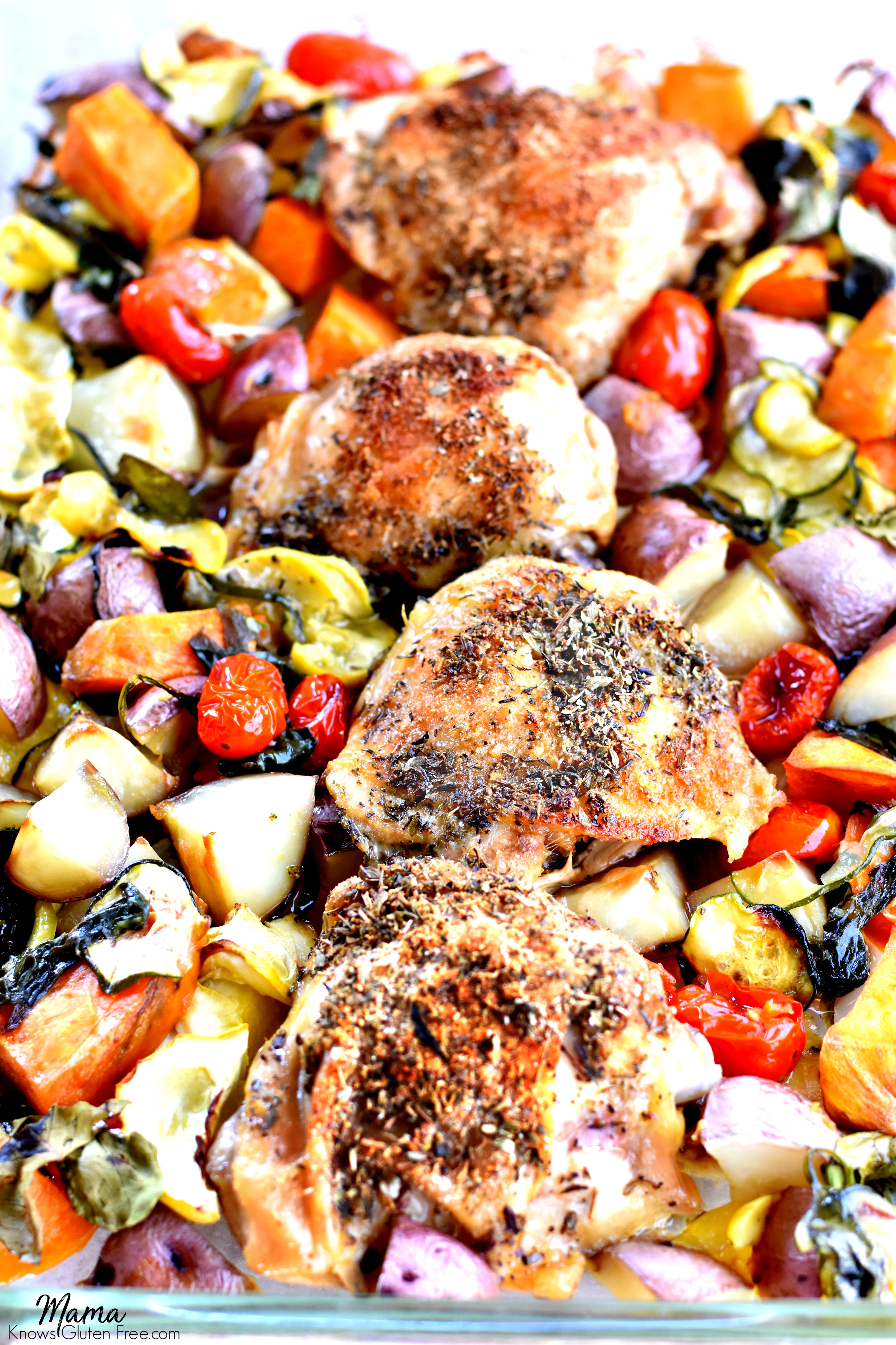 baked crispy chicken thighs with roasted vegetables in a glass baking pan