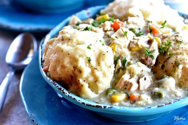 chicken and dumplings in a blue bowl with a sliver spoon