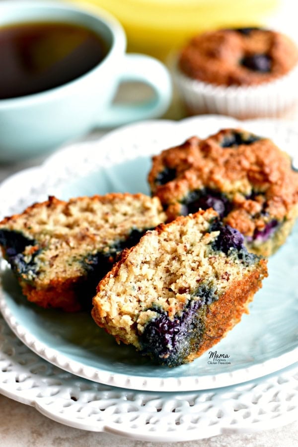 a Paleo banana blueberry muffins cu tin half to show the texture on a plate with another muffin and coffee and bananas in the background