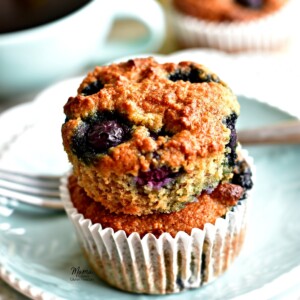 two Paleo blueberry banana muffins stacked on top of each other on a plate with a fork