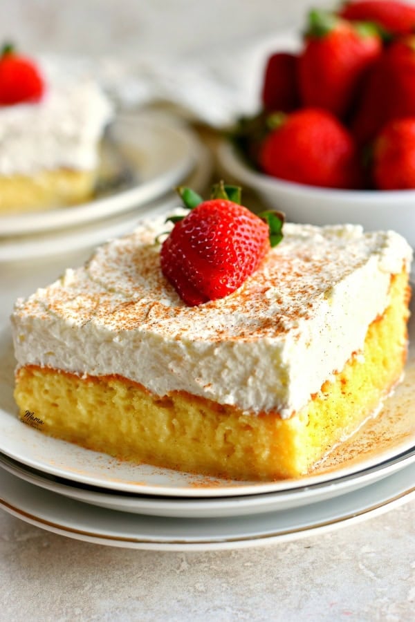 a slice Gluten-Free Tres Leches Cake on plate with another piece and strawberries in the background.