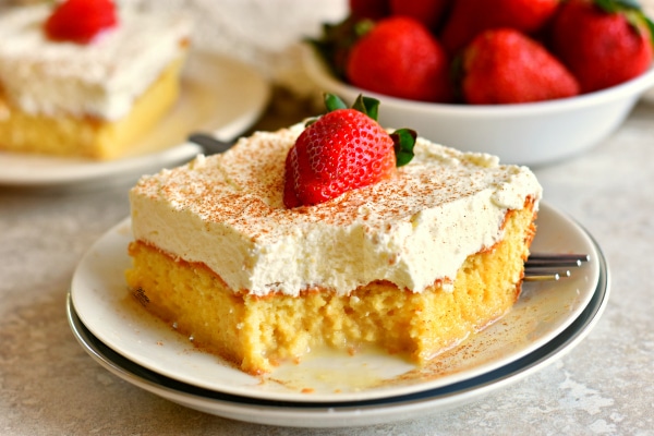 piece Gluten-Free Tres Leches Cake on a plate with strawberries and another slice in the background