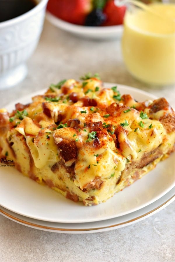 a serving of Gluten-Free Eggs Benedict Casserole on a plate with coffee, berries and hollandaise sauce in the background