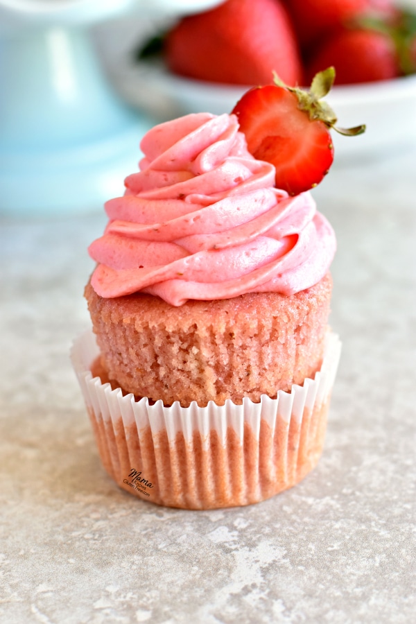 2 gluten-free strawberry cupcakes stacked on top of each other with a bowl of strawberries in the background