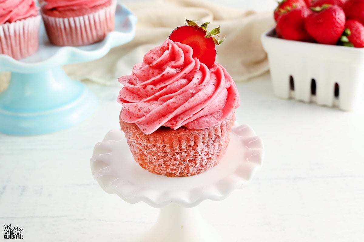 glutne-free cupcake on a white cupcake stand with the cupcakes and strawberries in the background