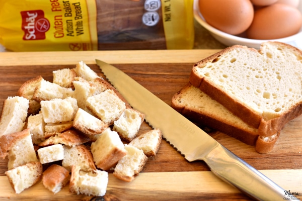 Schar gluten-free bread cutin to pieces and slices on a cutting board with a knife and the loaf and eggs in the background