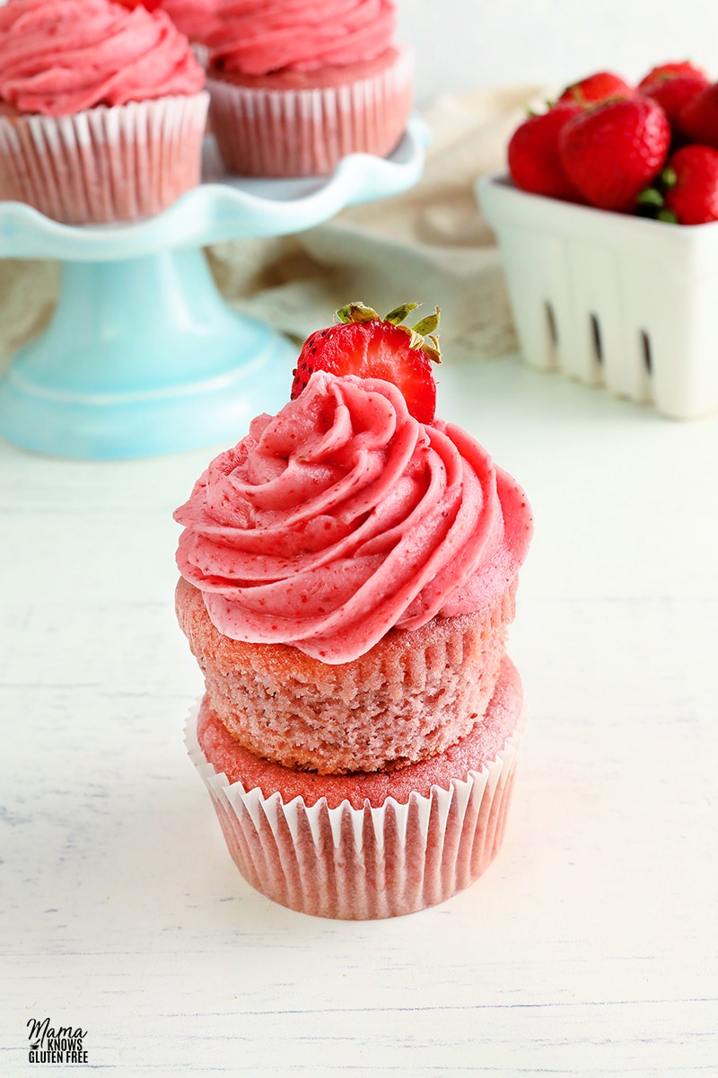 gluten-free strawberry cupcakes stacked on top of each other with the cupcakes and strawberries in the background