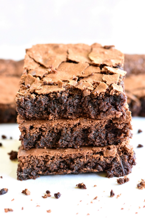 three gluten-free brownies stacked on top of each other with brownies in the background