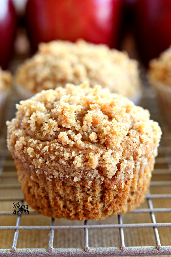 Easy Gluten_Free Apple Cinnamon Crumb Muffins on a cooling rack with apples in the background