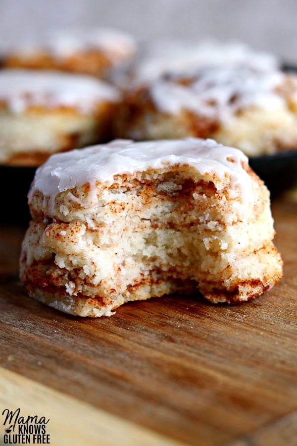 cinnamon roll biscuit with bite out o fit to show the texture. More cinnamon biscuits in the background in a cast iron skillet. 