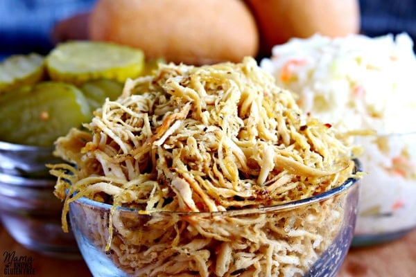 rotisserie style shredded chicken in a bowl, pickles in a bowl, coleslaw in a bowl and rolls