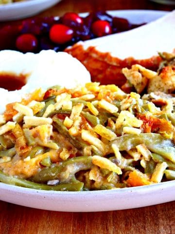 gluten-free cheesy green bean casserole ona plate with turkey, mashed potatoes, cranberry sauce.