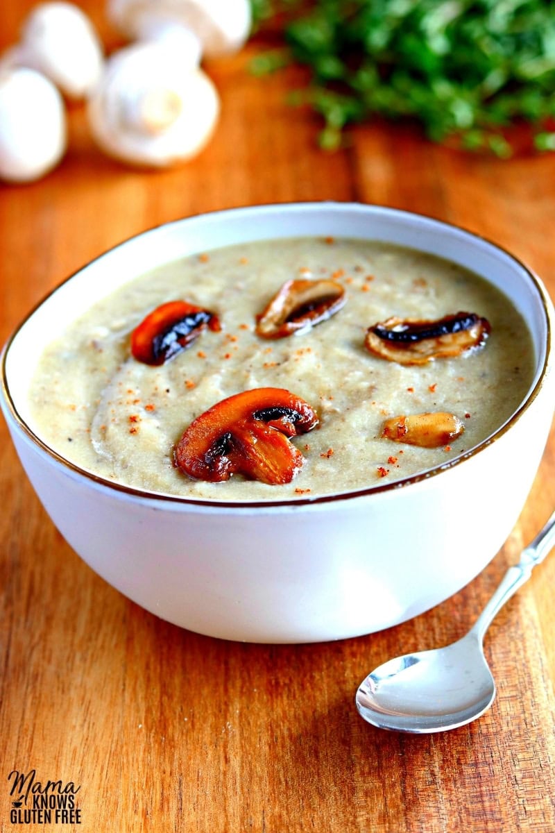 gluten-free cream of mushroom soup in a white bowl with and spoon and thyme and mushrooms in the background.