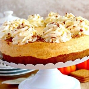 gluten-free pumpkin cheesecake on a cake stand with pumpkins, graham crackers and a teapot in the background.