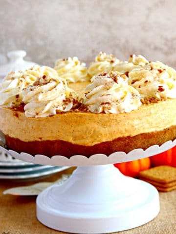 gluten-free pumpkin cheesecake on a cake stand with pumpkins, graham crackers and a teapot in the background.