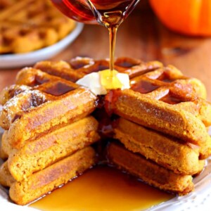 three gluten-free pumpkin waffels ona plate with syrup being poured on it