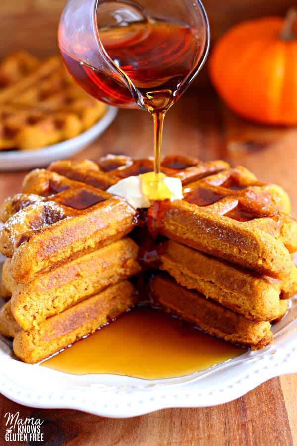 three gluten-free pumpkin waffles with butter and syrup being poured on it. 