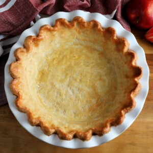 gluten-free pie crust baked in a white pie pan with a red napkin an apples in the background